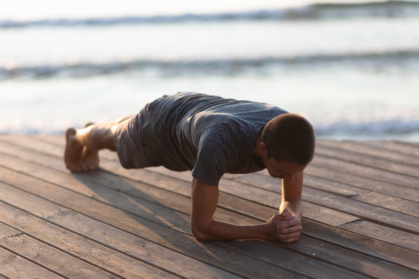 A man does plank exercise on a dock.