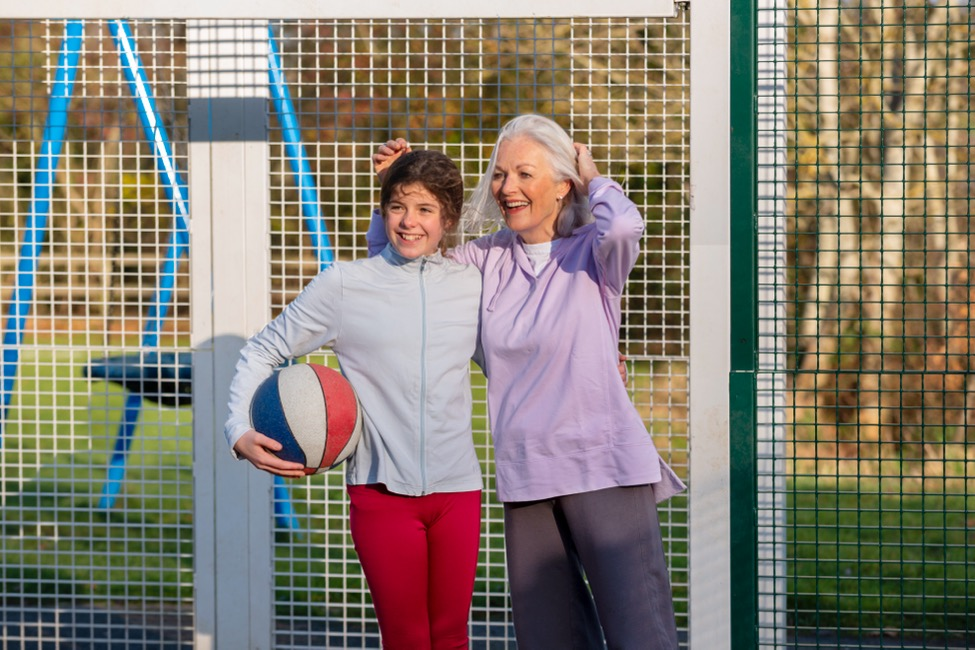 A grandmother and child holding a basketball stand in front of a park fence.