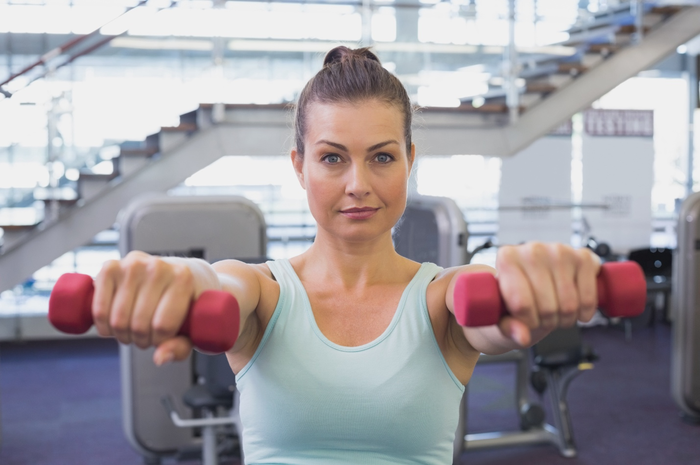  A woman holds two red dumbbells in front of her.