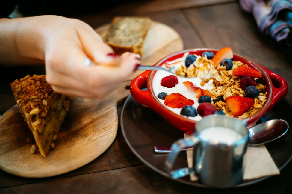 A person holds a spoon to eat a bowl of oats, berries, and yogurt.