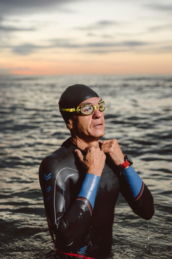 An older man wearing a wetsuit and goggles rests after swimming in the ocean.