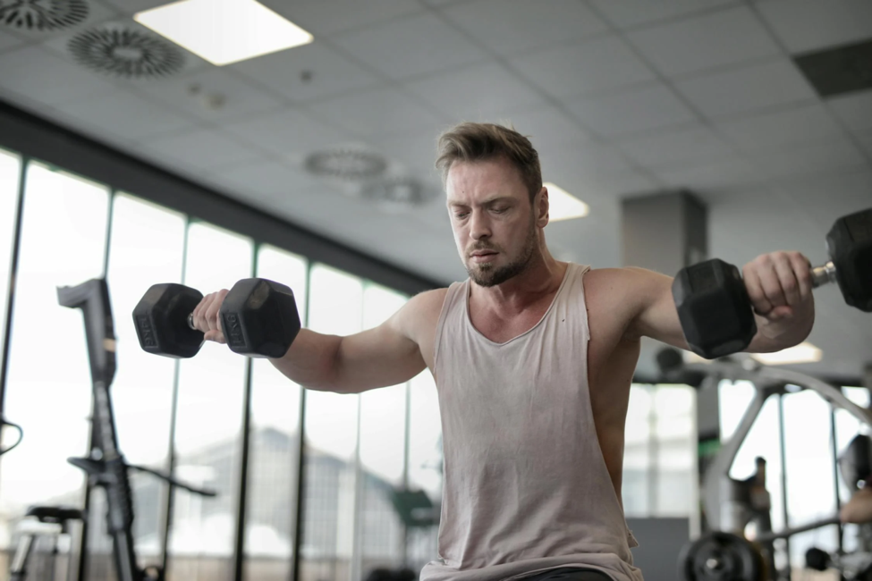 A man looks stressed out as he lifts heavy dumbbells.